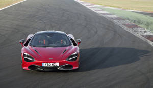 紅色McLaren 720S在賽道上奔馳，帶有輪胎痕跡和路緣。 — 4K 法拉利 壁紙
