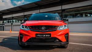 紅色Proton X50 SUV停放在賽道上，背景有現代建築。 — 超跑 壁紙