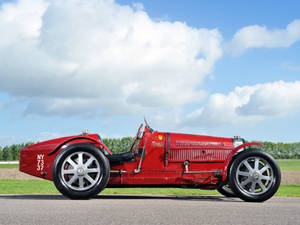 一輛經典紅色賽車停在有綠色田野和藍天的路上。 — Bugatti iPhone 壁紙
