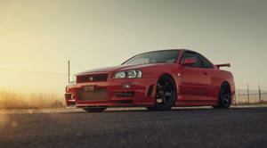 日落時紅色日產Skyline GT-R停在瀝青上，後面有圍欄。