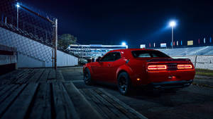 紅色肌肉車在夜間停在賽車場上，燈光明亮。 — 道奇挑戰者 壁紙