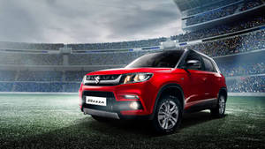 紅色鈴木 Brezza SUV 停在體育場上，四周是歡呼的球迷。 — 鈴木 壁紙