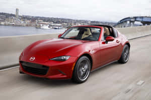 紅色馬自達MX-5敞篷跑車在靠近城市和橋樑的海岸公路上行駛。 — 馬自達 壁紙