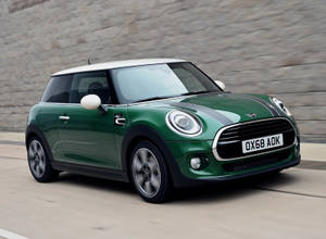 綠色Mini Cooper在石牆旁的柏油路上行駛。 — 霓虹車 壁紙