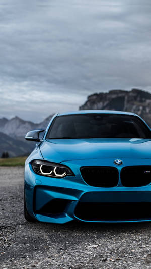 多雲天空下，碎石上靠近山巒的藍色BMW M2跑車 — 藍色美學電腦 壁紙