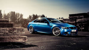 藍色BMW M3跑車停在堆疊木頭旁邊，夕陽西下。 — 福斯汽車 壁紙