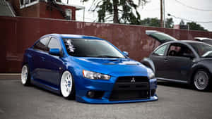 藍色改裝三菱Lancer Evolution停放在灰色金龜車旁邊，引擎蓋打開。 — JDM風格 壁紙