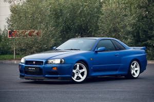 藍色日產R34 GTR跑車停在瀝青路上，靠近樹木。