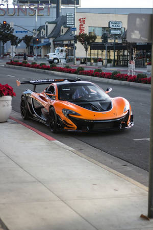 橙色McLaren P1 GTR停放在城市人行道上，靠近紅色聖誕紅和Sunset Plaza標誌。 — 麥拉倫 壁紙