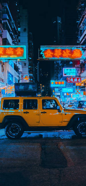 黃色吉普車停在繁忙亞洲城市夜晚的霓虹燈招牌下。 — iPhone 14 Pro Max 壁紙