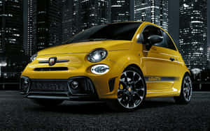 夜晚停放在城市街道上的黃色 Abarth Fiat 500，背景是燈火通明的摩天大樓。 — MacBook Pro 13 壁紙