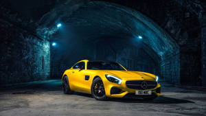 在光線昏暗的石隧道中，一輛黃色 Mercedes-AMG GT 跑車配上藍色聚光燈。 — Mercedes Benz C300 壁紙