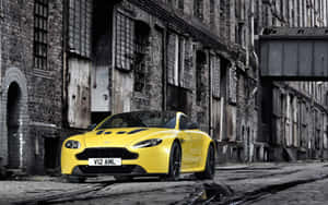 黃色Aston Martin停放在濕滑鵝卵石街道，靠近舊磚建築。 — Steam Deck OLED 壁紙