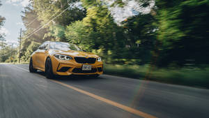 黃色BMW M2在陽光明媚的森林道路上疾馳，帶有動態模糊效果。 — Mercedes Benz C300 壁紙