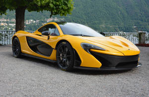 黃色McLaren P1超級跑車停在碎石路上，靠近湖泊，背景有山脈。 — 麥拉倫 壁紙