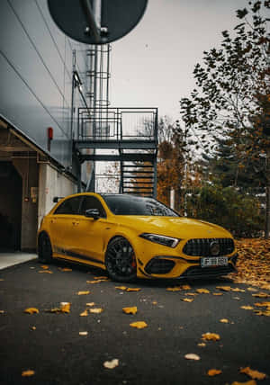 黃色Mercedes-AMG A45停放在靠近現代建築的、覆蓋著秋葉的瀝青路面上。 — 秋季 壁紙