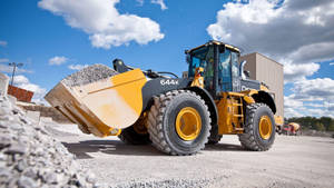 在藍天下的工地，黃色建築裝載機抬起碎石。