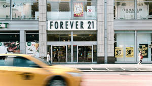 黃色計程車快速駛過帶有特價標誌的Forever 21零售店。 — 永遠21 壁紙