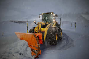 黃色鏟雪車在雪景山區道路上清除積雪。 — MacBook Pro M2 壁紙