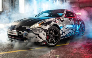 黑白迷彩日產370Z Nismo在煙霧瀰漫的車庫中漂移，帶有彩色燈光。 — 日產 壁紙