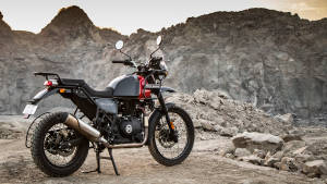 日落時分，一輛黑紅色的 Royal Enfield 摩托車停在岩石地形上。