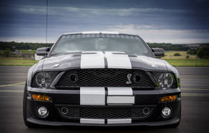 暴風雨天空下，賽道上的黑色 Shelby Mustang 帶有白色條紋。 — 野馬GIF 壁紙
