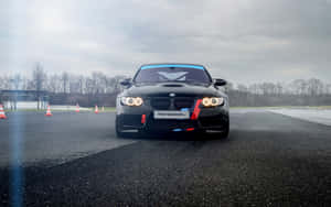黑色BMW M3賽車在陰天下濕賽道上的橙色錐筒旁。 — 2560x1600 壁紙