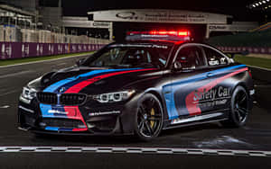 夜間潮濕賽道上帶有紅藍塗裝的黑色BMW M4安全車。 — MacBook Air M1 壁紙