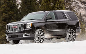 黑色GMC Yukon Denali在雪地行駛，背景有常綠樹。 — Steam Deck 壁紙