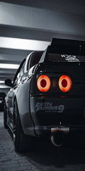 黑色日產Skyline R34在黑暗車庫中帶有發光的橙色尾燈。 — Pixel 3 壁紙
