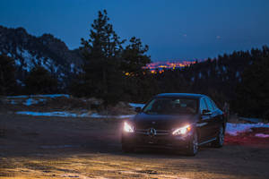 黑色賓士轎車車頭燈在暮色中照亮靠近山脈的雪泥路。 — Mercedes Benz C300 壁紙