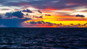色彩繽紛的雲彩和深色海面上的鮮豔日落 — 5120x2880 壁紙