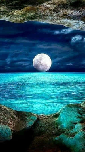 夜晚滿月映照碧綠海洋，岩石環繞 — 月夜星空 壁紙