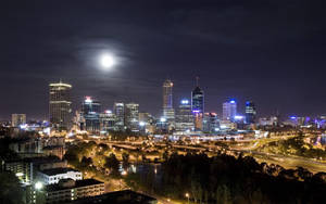 明亮的滿月下的夜間城市天際線，發光的建築物和道路。 — 城市 壁紙