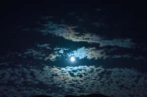 明亮的滿月在黑暗的夜空中透過散落的雲層發光。 — 月光 壁紙