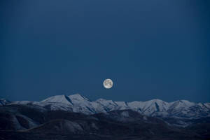 滿月在夜間從積雪的山峰上升起。 — 高畫質月亮 壁紙