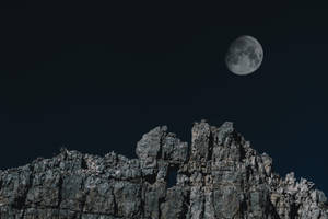 滿月在夜間從尖銳的岩石山峰上升起。 — 高畫質月亮 壁紙