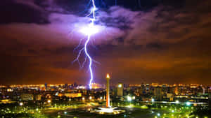 閃電照亮夜間的城市天際線，中央有一座紀念碑。 — 印尼 壁紙