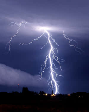 強大的閃電照亮了鄉村景觀上空的暴風雨之夜，遠處有燈光。 — 閃電 壁紙