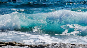 碧綠色海浪撞擊深色岩石，白色泡沫飛濺 — 海灘 壁紙