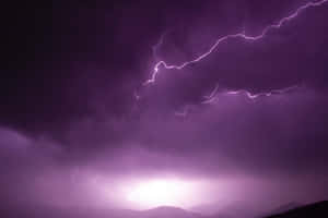 紫色閃電照亮了山脈剪影上方的暴風雨夜空。 — 暗紫色美學 壁紙