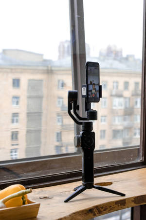 黑色雲台穩定器在木製窗台上拿著手機，俯瞰城市建築。 — 酷炫 iPad 壁紙