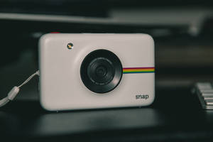 帶有彩虹條紋的白色Polaroid Snap相機，深色桌子上，旁邊有鍵盤。 — 日式自然壁紙