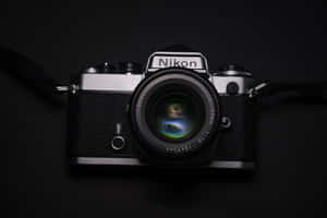 復古 Nikon 底片相機配備 50mm 鏡頭，在黑色背景上反射彩色光線。 — Kodak Black 壁紙