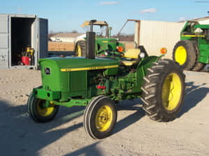 綠色John Deere拖拉機停放在礫石上，靠近農場設備和建築物。 — 老福特卡車 壁紙