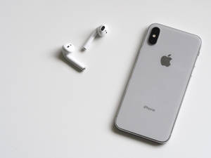 銀色 iPhone X 和白色 AirPods 在白色表面上。 — 酷炫iPhone 壁紙