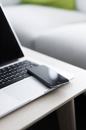 銀色筆記型電腦和黑色電話在木桌上，靠近白色沙發。 — MacBook Air 壁紙
