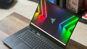 木桌上的黑色 Razer 筆記型電腦，帶有霓虹發光螢幕桌布。 — 筆電 壁紙