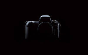 一部黑色Nikon F100相機機身置於黑暗中央，帶有微妙高光。 — 深色模式 壁紙