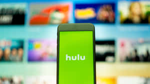 智慧型手機顯示 Hulu 應用程式標誌，背景為模糊的電視螢幕。 — iMac 壁紙